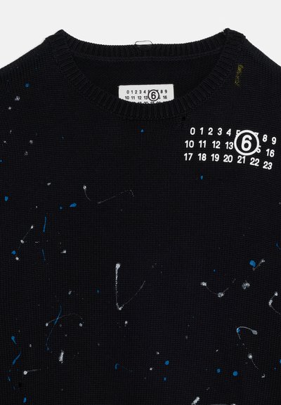 Μαύρο πλεκτό πουλόβερ με πιτσιλιές από μπλε και λευκή μπογιά, με λευκό γραφικό ενός αριθμημένου πλέγματος με τον αριθμό 6 κυκλωμένο στο στήθος.