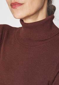 Suéter de cuello alto de canalé en color burdeos con un diseño ceñido al cuerpo y cuello alto. Textura suave con un ligero brillo y detalles de canalé estructurado.