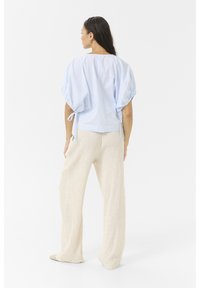 Light blue striped blouse with puff sleeves and ties, paired with cream wide-leg pants. Smooth fabric with a relaxed fit, minimal detailing.