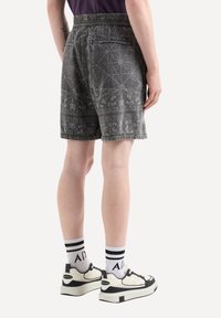 Pantaloni corti grigi con motivo, dotati di cintura elastica, caratterizzati da design dettagliati, una tasca posteriore, indossati con scarpe da ginnastica bianche e nere e calzini a righe.