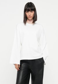 White long-sleeve shirt with a round neckline and loose fit, paired with black leather pants. Soft texture, minimalistic design, no patterns.