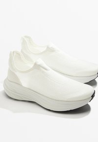 Biele slip-on tenisky s texturovaným pleteným vrchom, hrubou polstrovanou podrážkou a minimalistickým dizajnom. Čierna podrážka zvýrazňuje bielu farbu.