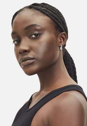 Model met gevlochten haar draagt een zwart mouwloos topje. Heeft zilveren oorringen en een neutrale huidtint, waarmee natuurlijke schoonheid wordt getoond.