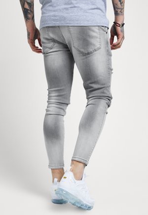 Grijze denim skinny jeans met gescheurde details, gecombineerd met witte sneakers met een doorzichtige zool en gele accenten.