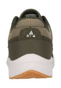 Grön atletisk sko med ett texturerat mesh-övre, en solid hälkopp och en vit mellansula med en orange sula. Logodetalj på hälen.