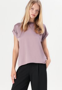 Light purple short-sleeve top with a relaxed fit. Smooth, textured fabric and subtle curved hem. Paired with black wide-leg pants.