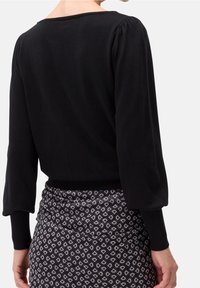 Schwarzer Pullover mit Rundhalsausschnitt und gepufften Ärmeln, kombiniert mit einem gemusterten Rock mit einem geometrischen Design in dunklen Tönen.