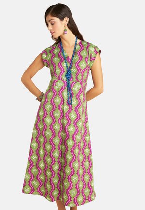 Woman wearing green and purple patterned midi dress with short sleeves, paired with blue beaded necklace and colorful earrings and bracelets.