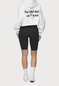 Sudadera blanca corta con texto negro en la parte de atrás y pantalones cortos de ciclismo negros. Calcetas blancas y zapatillas completan el conjunto.