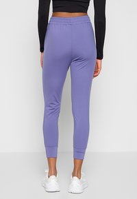 Jasnofioletowe, zwężane dresy wykonane z gładkiego, elastycznego materiału z elastycznym paskiem w talii i prążkowanymi mankietami, połączone z białymi sneakersami.