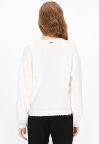 Witte, oversized trui met een zachte, pluizige textuur. Heeft lange mouwen en een ontspannen pasvorm, afgewerkt met geribbelde boorden en een zoom.
