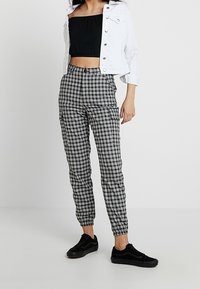 Svart och vit rutiga cargo-byxor med elastiska mudd, kombinerade med en svart kort topp och en vit denimjacka, bärs med svarta sneakers.