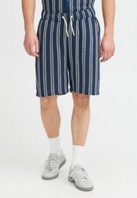Marine-stribede shorts med en struktureret stof, elastisk talje og cremede snore. Båret med grå sneakers og hvide ankelsokker.