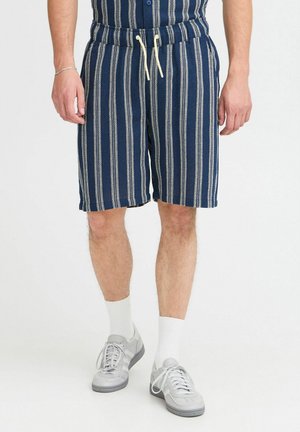 Marine gestreifte Shorts aus Textil mit einem elastischen Bund und einer cremefarbenen Schnur. Kombiniert mit grauen Sneakers und weißen Socken.