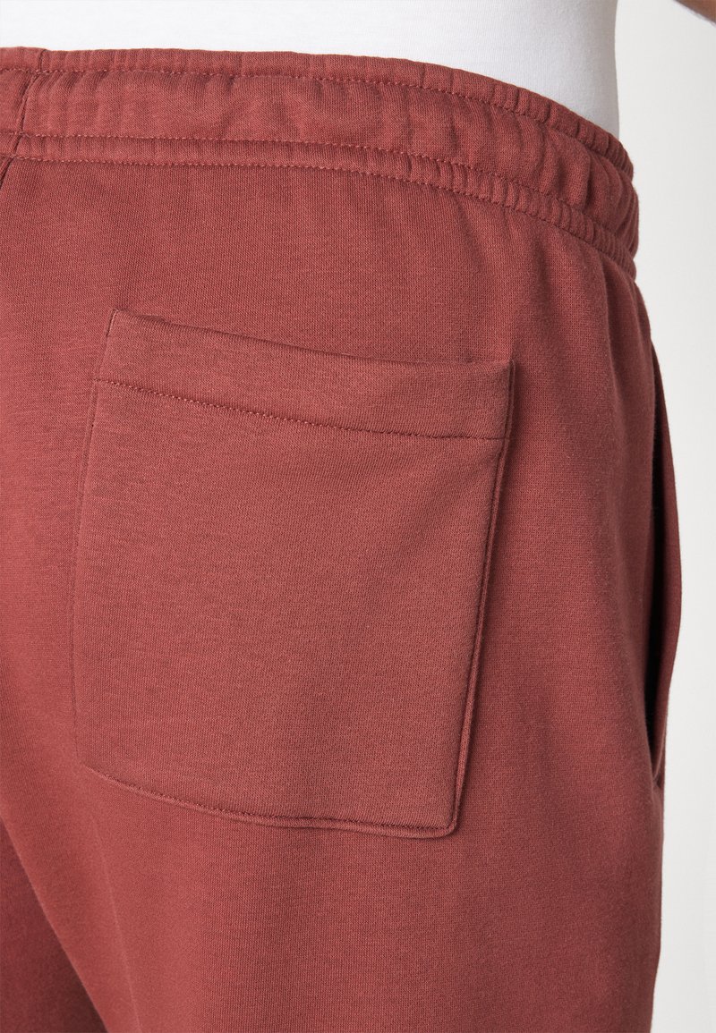 Marsala-farbene Jogginghosen aus strukturiertem Stoff, mit Gummizugbund und einer aufgesetzten Tasche auf der Rückseite für zusätzlichen Komfort.