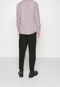 Červeno-bílá kostičkovaná košile s dlouhým rukávem, bavlněná tkanina, s knoflíkovými manžetami, spárovaná s černými zúženými kalhotami a lesklými černými botami.