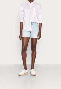 Ljusrosa och vita randiga skjortor med knappar, med en enkel bröstficka, tillsammans med fransiga jeansshorts och vita sneakers med beige sulor.