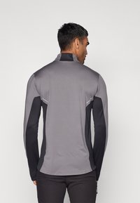 Maglietta sportiva a manica lunga con corpo grigio testurizzato, maniche nere, colletto alto e dettagli riflettenti lungo le cuciture.