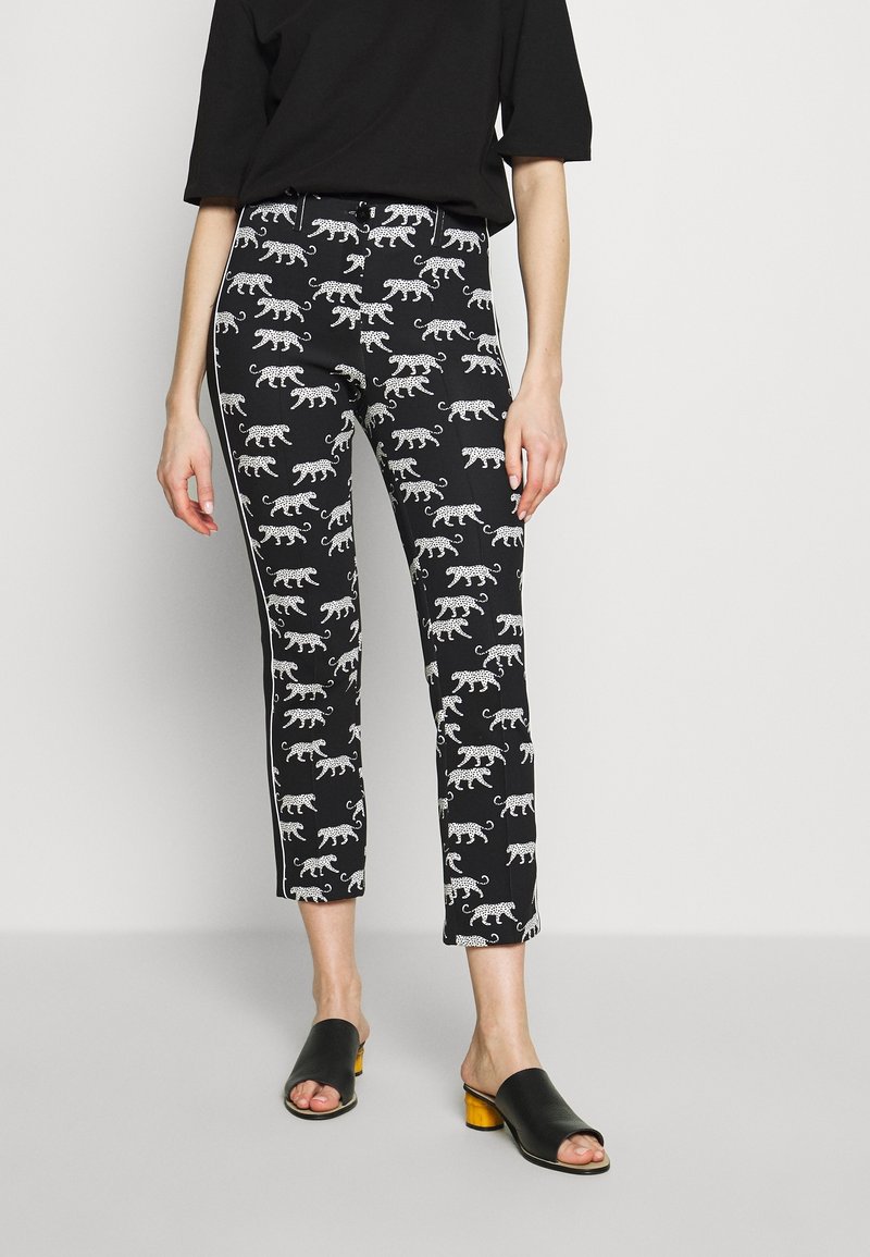 Femme portant un pantalon court noir à imprimé léopard blanc, un haut noir et des mules noires ouvertes avec talons blocs jaunes.