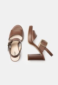 Brown leather platform sandals with a wide strap, adjustable buckle, and a chunky heel. Smooth texture and modern design.
