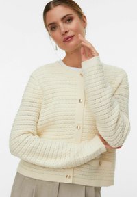 Cardigan in maglia crema con righe orizzontali, colletto e polsini a coste e grandi bottoni frontali. Texture morbida con dettagli sottili.