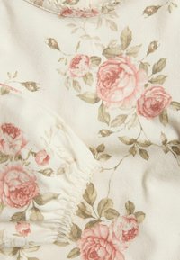 Blomsterpræget stof med pink roser og grønne blade på en cremet baggrund. Elastisk detalje langs sømmen. Blød tekstur.