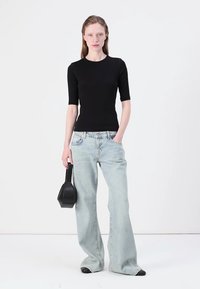 Sort tætsiddende t-shirt med korte ærmer kombineret med lyseblå bredbenede jeans. Modellen holder en sort geometrisk håndtaske. Glat stof, afslappet stil.