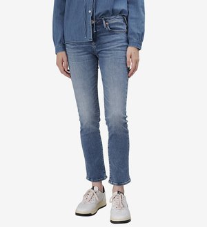 Jean en denim bleu clair avec une coupe ajustée et un léger effilochage à l'ourlet, associé à des baskets blanches avec des accents noirs et des détails texturés.