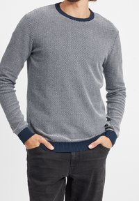 En strukturerad pullovertröja i marinblått och ljusgrått, med rund hals och ribbade ärmslut och nederkant. Mönstret liknar små diamanter.