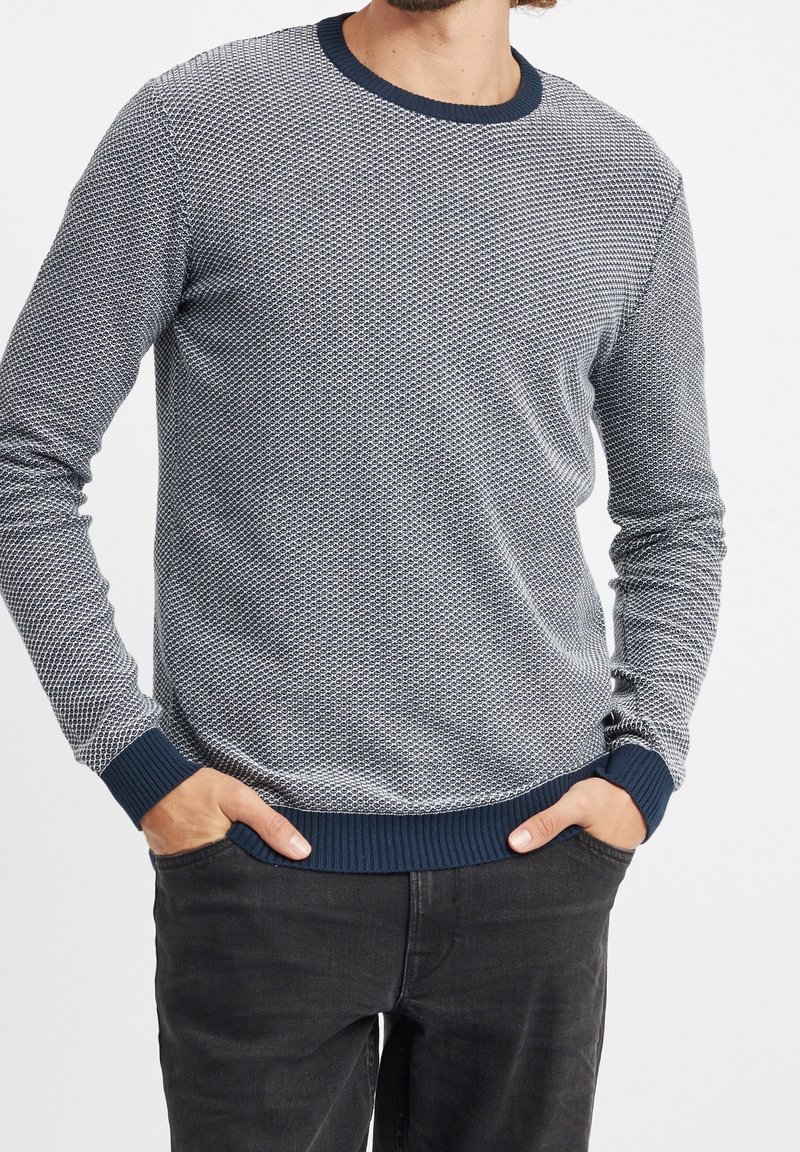 En strukturerad pullovertröja i marinblått och ljusgrått, med rund hals och ribbade ärmslut och nederkant. Mönstret liknar små diamanter.