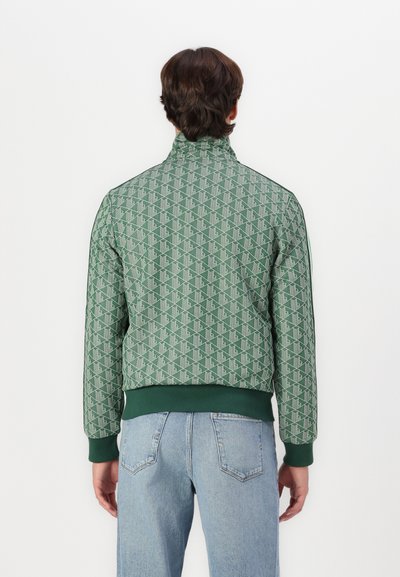 Veste bomber verte avec un motif géométrique, col haut, poignets et ourlet élastiques. Stylée avec un jean bleu clair, vue de dos.