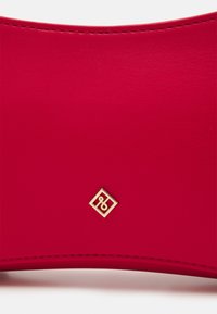 Hladký povrch z červené kůže s zakřivenými okraji a malým zlatým geometrickým emblémem umístěným blízko spodního okraje.