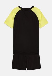 Svart sportoutfit med T-shirt med kort ärm och gula raglanärmar samt matchande svarta shorts; tillverkad av lätt och ventilerande tyg.
