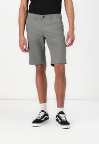 Gray cotton shorts with a straight cut, front pockets, and a button closure, paired with black sneakers and white socks.