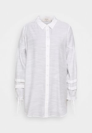 Longue blouse blanche à boutons avec col pointu, tissu texturé, manches froncées et liens ruban aux poignets.