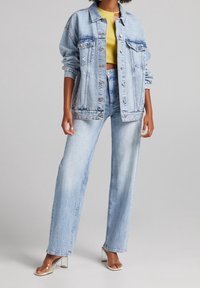 Ljusblå denimjacka med oversized passform, framfickor och metallknappar, kombinerad med högmidjade ljusblå jeans och klara klacksandaler.