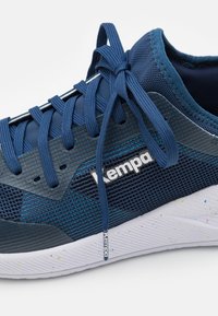 Tengerészkék hálós sportcipő, textúrázott dizájnnal, fehér logóval és fűzővel, valamint kontrasztos fehér talppal, mely színes pöttyöket tartalmaz.