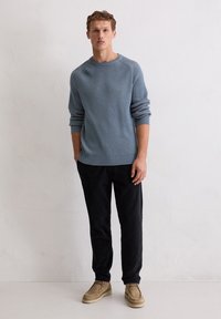 Lichtblauwe gebreide trui met een textuurpatroon, ronde halslijn en opgerolde mouwen, gecombineerd met zwarte broek en beige schoenen.