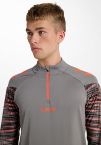 Graues sportliches Oberteil mit kurzem Reißverschluss, orangefarbenen Akzenten und gemusterten Ärmeln. Verfügt über ein Logo in der Mitte und ein hohes Kragen-Design.