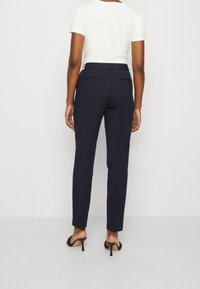 Navy kalhoty na míru s úzkým střihem, které mají zadní kapsy a hladkou texturu. V kombinaci s bílou košilí s krátkým rukávem a černými lodičkami.