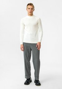 Witte lange mouwen crewneck trui van textiel met structuur, gecombineerd met grijs gestreepte broek met opgerolde boorden en zwarte schoenen.