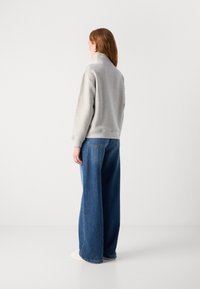 Grå sweatshirt med hög hals, långa ärmar och avslappnad passform. Matchad med vida blå jeans och vita skor. Enkel och avslappnad design.