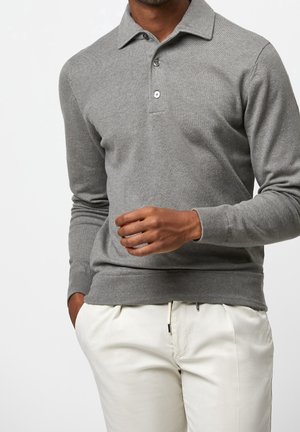 Grauer Strick-Poloshirt mit langen Ärmeln und klassischem Kragen, ausgestattet mit drei Knöpfen und gerippten Bündchen. Kombiniert mit hellfarbigen Hosen.