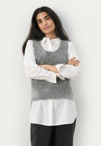 Grijze donzige gebreide vest met een ronde hals, gedragen over een witte blouse. Het vest heeft een comfortabele pasvorm en een gestructureerde uitstraling.