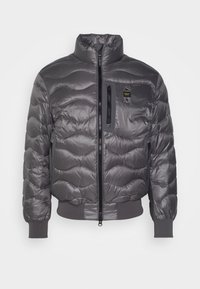 Giubbotto puffer grigio con design trapuntato, colletto alto, zip frontale e tasca sul petto; presenta polsini e vita a coste, tessuto morbido.