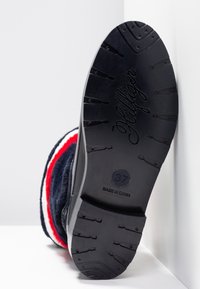 Semelle de bottes en caoutchouc noir avec une surface texturée antidérapante, côtés en tissu bleu marine et accents rouge et blanc. Taille 37 estampillée à la base.