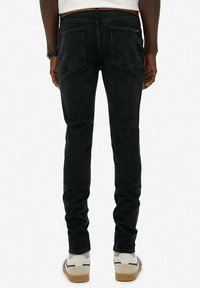 Vaqueros de mezclilla negra con un corte ajustado, que presentan bolsillos traseros y un acabado limpio. Llevados con zapatillas blancas, mostrando un diseño minimalista.