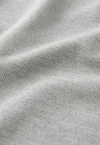 Primer plano de una tela gris texturada, con un patrón tejido que presenta una superficie suave, ligeramente irregular y sutiles variaciones en el tono.