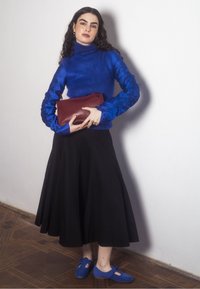 Niebieski sweter w golf z teksturowanymi niebieskimi rękawami, czarna zwiewna spódnica i niebieskie buty z wycięciem. Trzyma czerwoną kopertówkę.