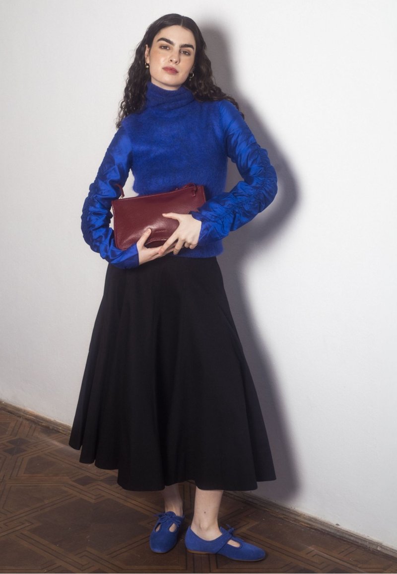 Niebieski sweter w golf z teksturowanymi niebieskimi rękawami, czarna zwiewna spódnica i niebieskie buty z wycięciem. Trzyma czerwoną kopertówkę.